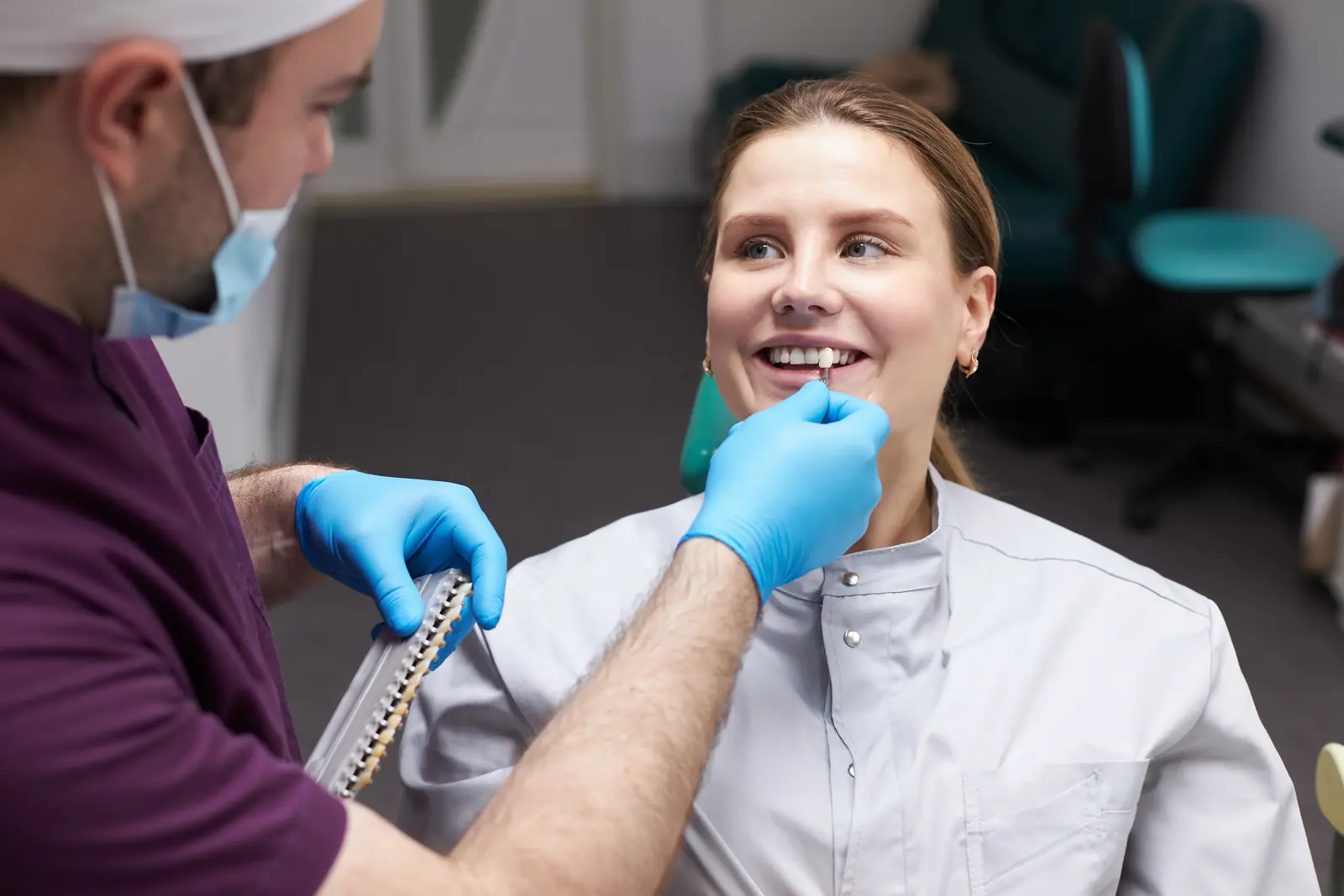 A dentist holding a tooth shade guide up to a smiling patient’s teeth
