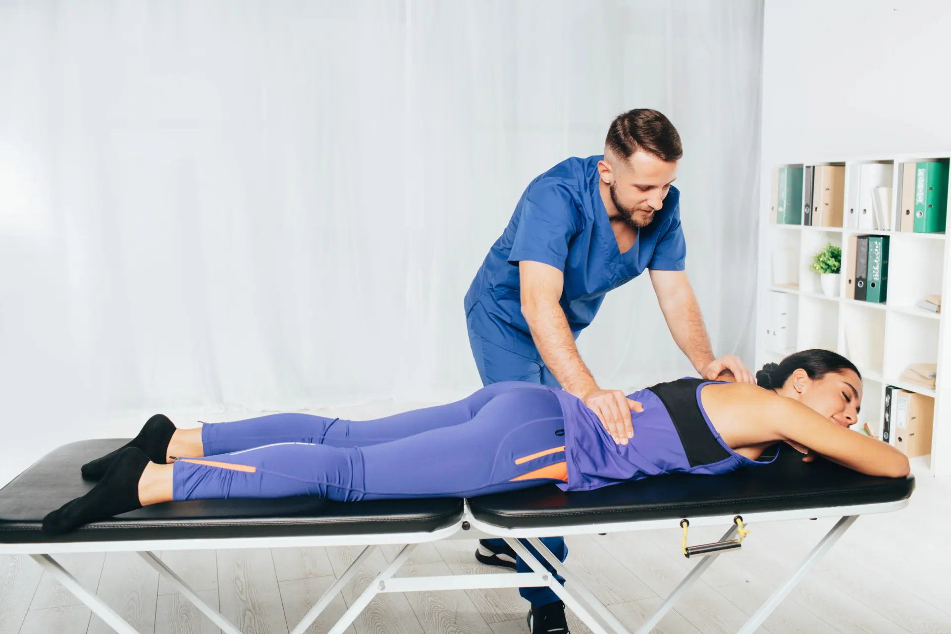 A clinician applying hands-on pressure to the back of a patient lying face down on a treatment table