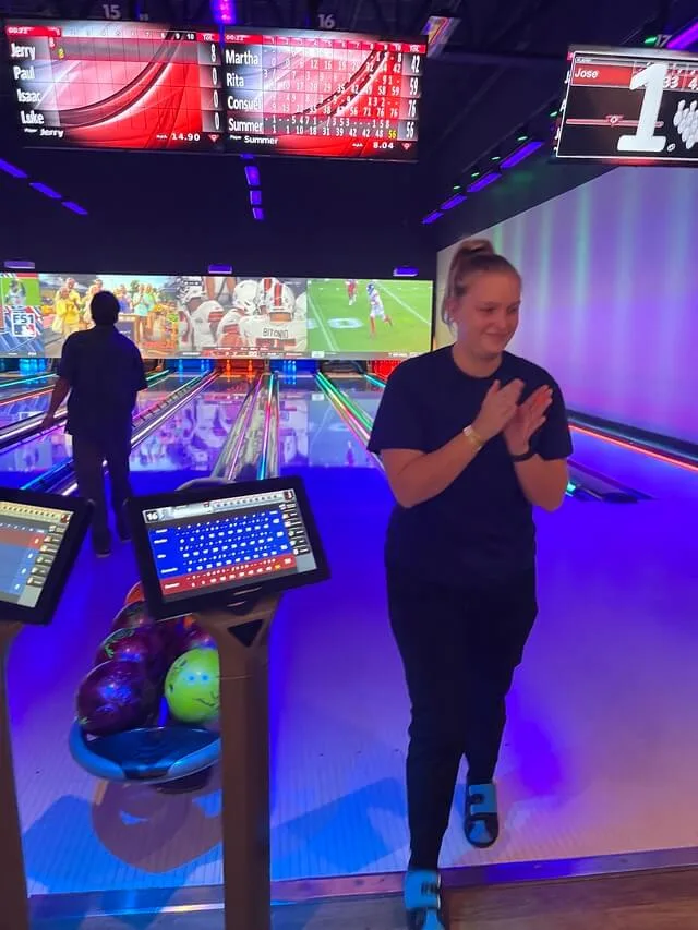 Woman clapping and smiling at bowling alley with scoreboards lit