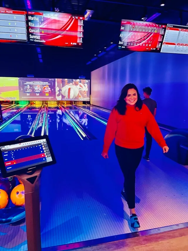 Smiling woman in red sweater at bowling alley with scoreboards
