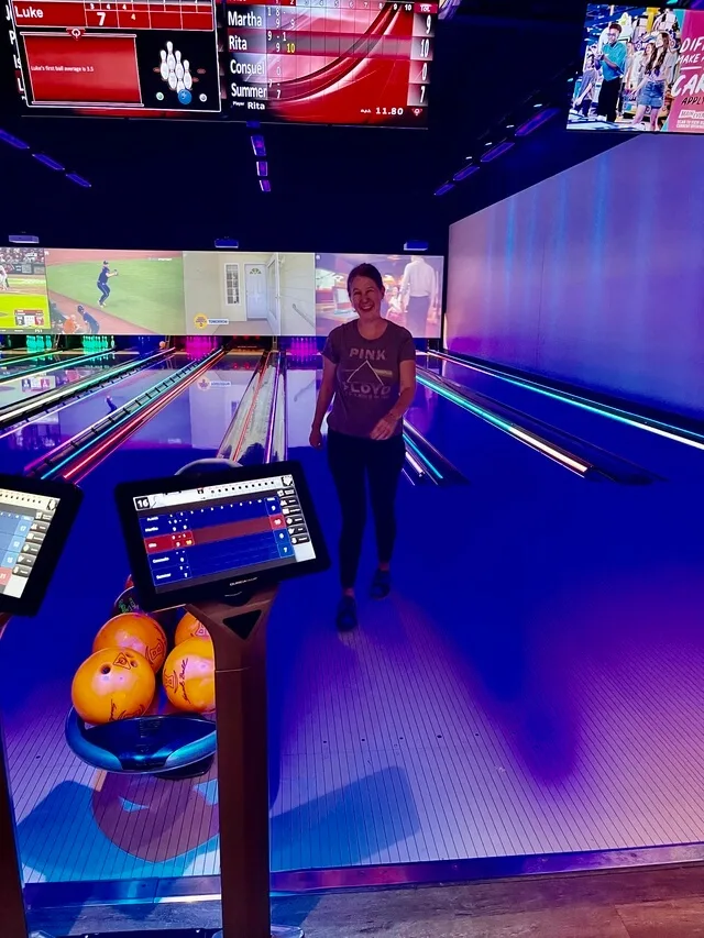 Smiling woman in bowling alley standing near lanes and screens
