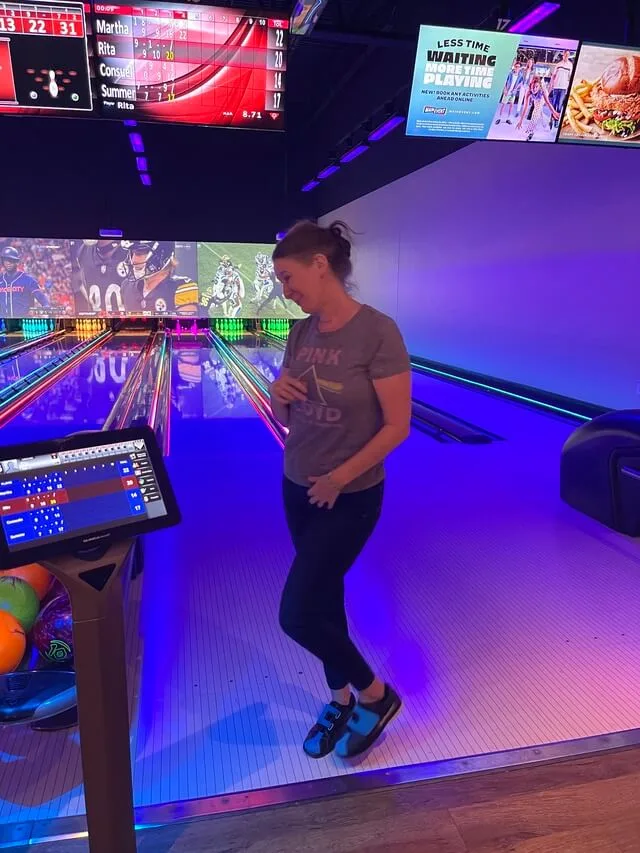 Woman smiling and pointing while standing at bowling alley lane