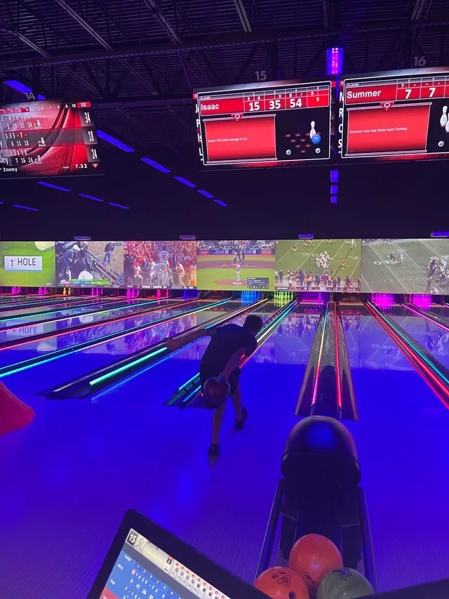Person bowling under neon lights with scoreboards overhead