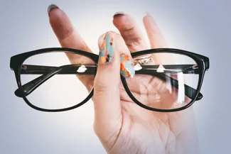 Hand holding modern eyeglass frames against light background