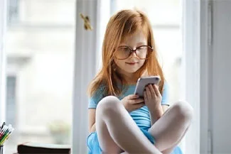 Smiling girl with glasses reading a book indoors by window